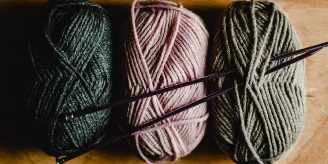 Drei Knäuel Wollgarn mit Stricknadeln auf Holz