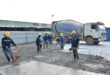 Bauarbeiter glätten frisch gegossenen Beton auf einer Fläche, im Hintergrund ein Fahrmischer