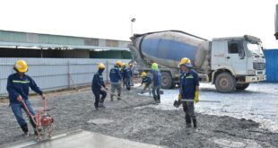 Bauarbeiter glätten frisch gegossenen Beton auf einer Fläche, im Hintergrund ein Fahrmischer