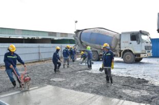 Bauarbeiter glätten frisch gegossenen Beton auf einer Fläche, im Hintergrund ein Fahrmischer