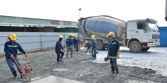 Bauarbeiter glätten frisch gegossenen Beton auf einer Fläche, im Hintergrund ein Fahrmischer