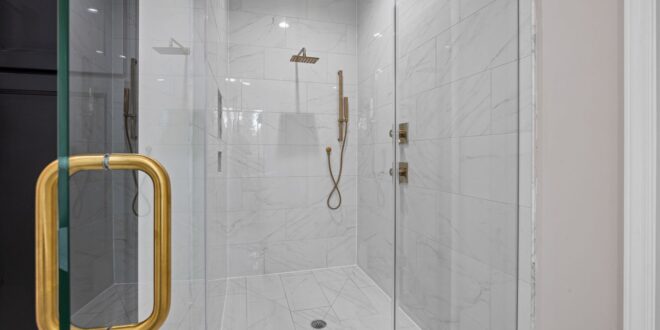 Geflieste Dusche mit Glaswänden und Bodenablauf auf Höhe des Badbodens