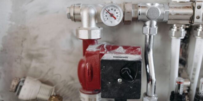 Heizungsverteiler mit roter Umwälzpumpe, Thermometer und Rohrleitungen an einer Wand