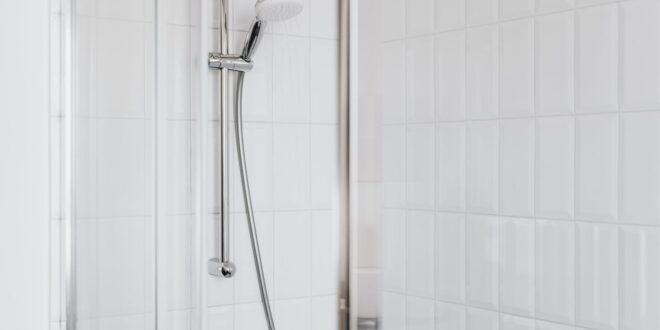 Duschbereich mit weißen Wandfliesen, Brausestange und Glaswand