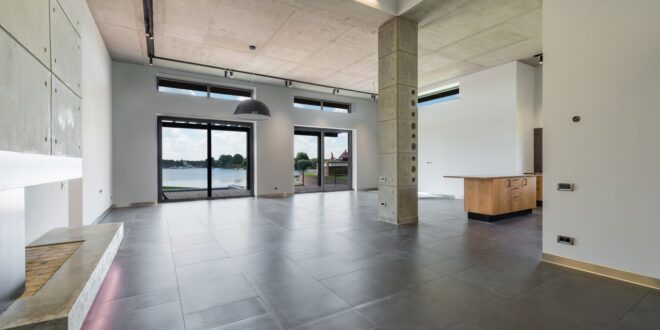 Leerer Wohnraum mit grauem Fliesenboden, Betonsäule und großen Fenstern
