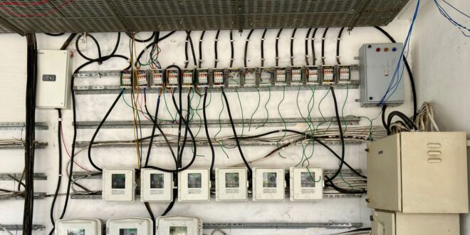 Elektroverteilung an einer Wand mit mehreren Stromzählern, Klemmenreihen und Kabeln