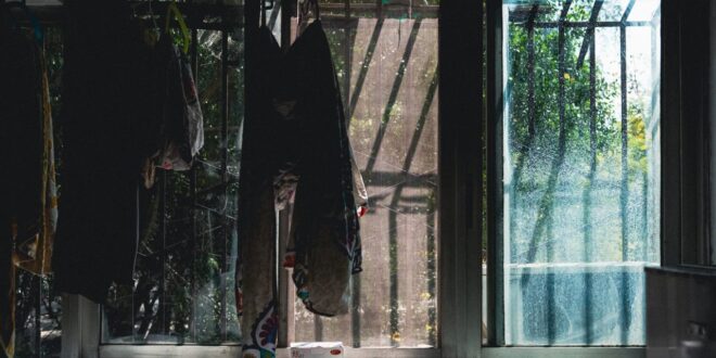 Sonnenlicht fällt durch große Glasschiebetüren in einen dunklen Raum, davor hängen Tücher