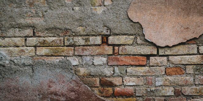 Alte Backsteinwand mit abgeplatztem Putz und freiliegenden Ziegeln