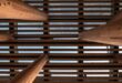 Tragwerk aus Holzstützen und dichter Reihe von Holzbalken, von unten gegen den Himmel fotografiert