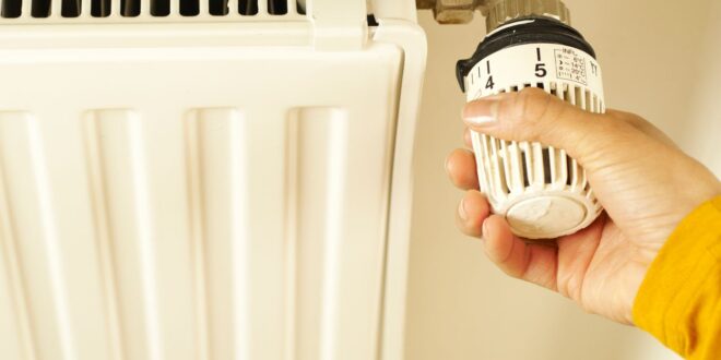 Hand dreht an einem Thermostatkopf eines weißen Heizkörpers