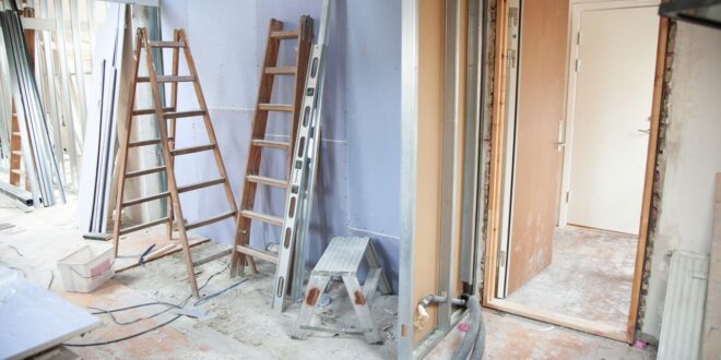 Wohnung im Umbau mit Trockenbau-Ständern, Leitern und freigelegtem Boden vor einer Tür