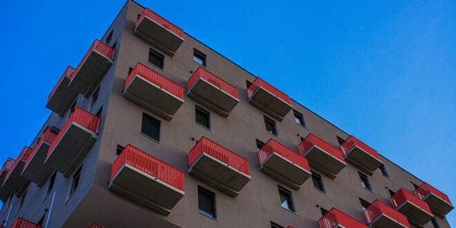 Mehrgeschossiges Wohnhaus mit roten Balkonen vor blauem Himmel, von unten gesehen