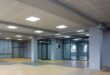 Große Halle mit abgehängter Rasterdecke aus hellen Platten und eingebauten LED-Panels, graue Stützen