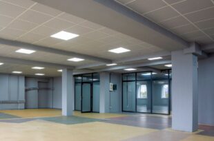 Große Halle mit abgehängter Rasterdecke aus hellen Platten und eingebauten LED-Panels, graue Stützen