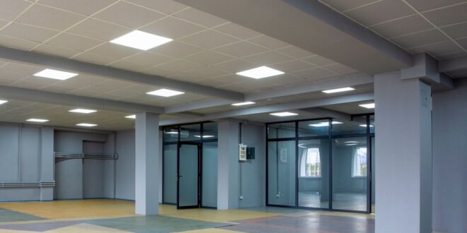 Große Halle mit abgehängter Rasterdecke aus hellen Platten und eingebauten LED-Panels, graue Stützen