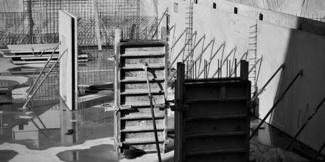 Schwarzweißfoto einer Rohbau-Baustelle mit Schalungselementen, Bewehrungsgittern und Betonwänden