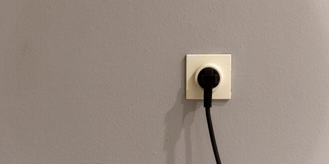 Steckdose mit eingestecktem Schutzkontakt-Stecker an einer grauen Wand
