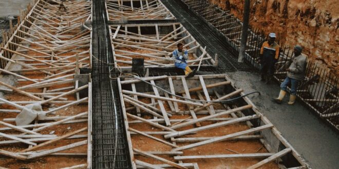 Baugrube mit Bewehrung und Schalung für eine Bodenplatte, Arbeiter im Hintergrund