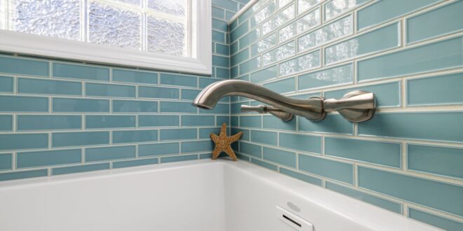 Weiße Badewanne mit Armatur an einer gefliesten Wand, Anschlussfuge zwischen Wanne und Fliesen