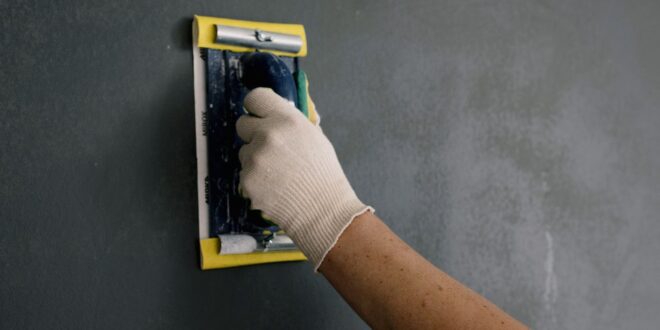 Hand mit Schleifklotz glättet eine gespachtelte Wand