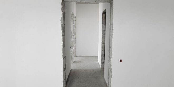 Rohbau-Türöffnung in einer verputzten Wand mit Blick in einen Flur ohne Boden- und Wandbelag