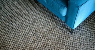 Grob gewebter, grau-brauner Teppichboden in Berber-Optik mit der Ecke eines blauen Sofas