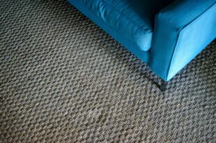 Grob gewebter, grau-brauner Teppichboden in Berber-Optik mit der Ecke eines blauen Sofas