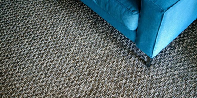 Grob gewebter, grau-brauner Teppichboden in Berber-Optik mit der Ecke eines blauen Sofas