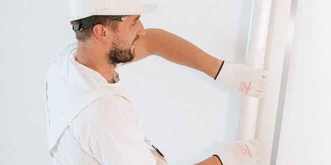 Handwerker mit Helm spachtelt eine Trockenbauwand glatt