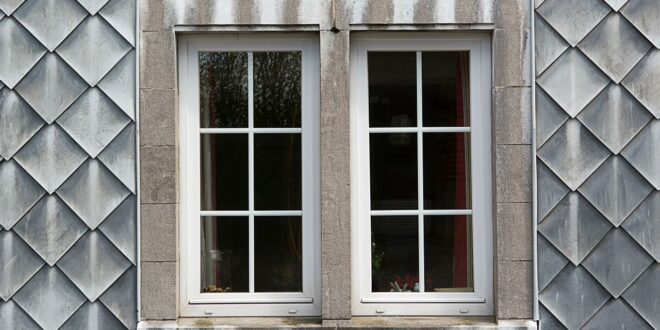 Zwei weiße Kunststofffenster mit Sprossen in einer grauen Schieferfassade