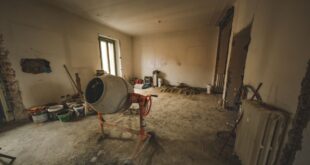 Entkernter Raum mit rauem Bodenuntergrund, Betonmischer, Farbeimern und einem alten Heizkörper während der Renovierung