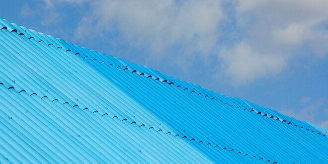 Blau lackierte Wellblech-Dachfläche mit zwei Dachseiten vor blauem Himmel mit Wolken