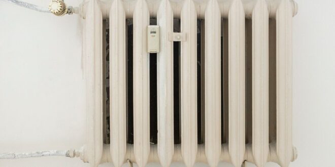 Weißer Gussheizkörper mit Thermostatventil an einer hellen Wand