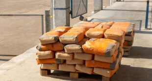 Gestapelte Zementsäcke mit orangefarbenem Aufdruck auf einer Holzpalette im Freien