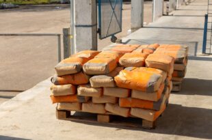 Gestapelte Zementsäcke mit orangefarbenem Aufdruck auf einer Holzpalette im Freien