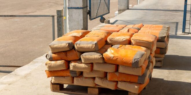 Gestapelte Zementsäcke mit orangefarbenem Aufdruck auf einer Holzpalette im Freien