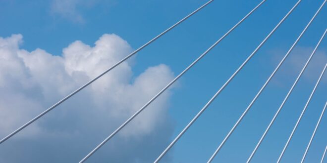 Weiße Stahlseile einer Schrägseilbrücke vor blauem Himmel