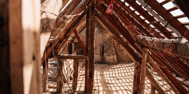 Offener Dachstuhl mit freiliegenden Holzsparren in einem unausgebauten Dachboden, Licht fällt durch die Dachfläche